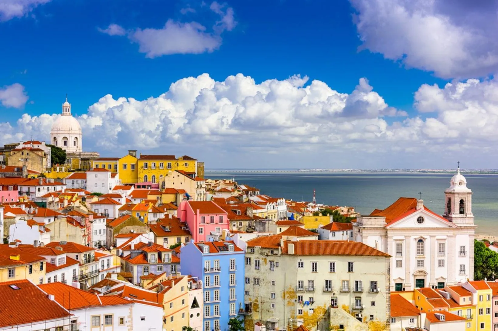 View over Alfama's terracotta rooftops from a miradouro, with the white dome of the National Pantheon on the left and the Tagus estuary behind